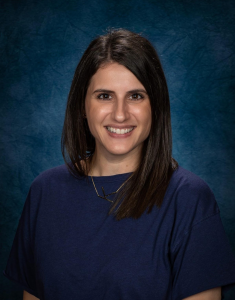 a woman with dark hair and a purple shirt smiles at the camera