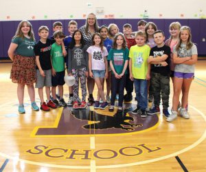 a woman stands in the middle of young students to pose for a picture in a gymnasium