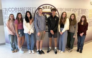 eight high school students pose in front of their school logo