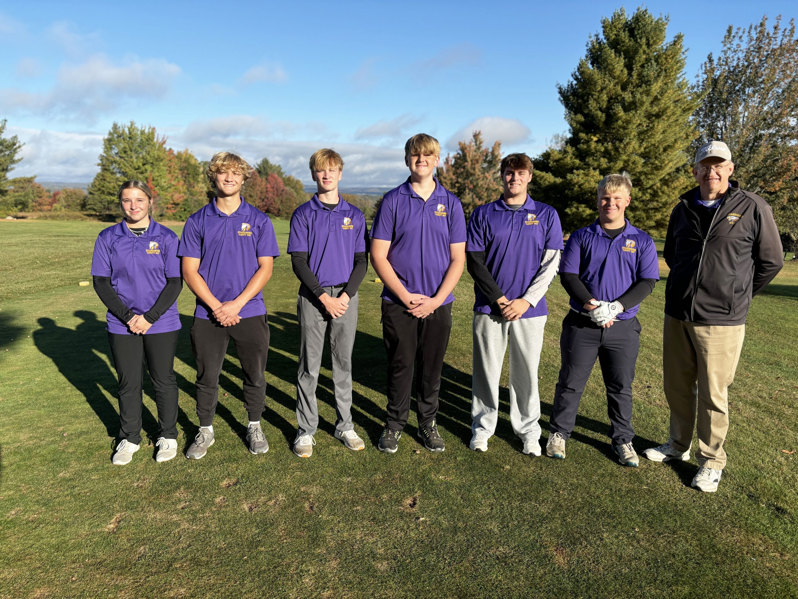 a golf team wearing purple shirts poses on a tee box