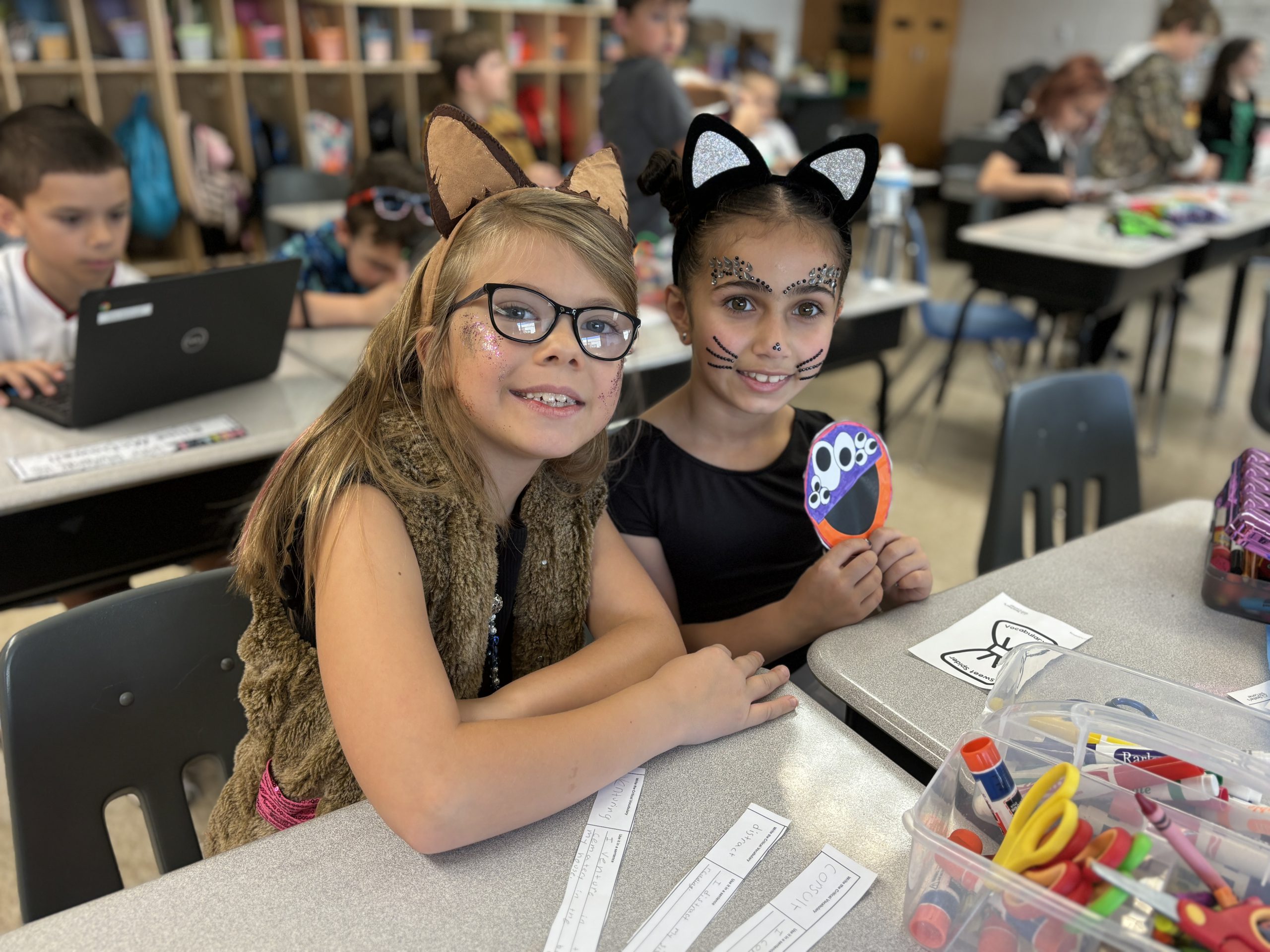 two young girls dress as animals for Halloween while sitting at their desk in school doing work