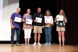 teachers hold certificates on a theatrical stage.