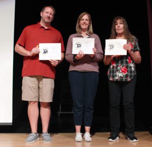 three teachers hold certificates on a stage.