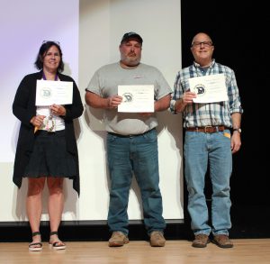 three adults hold certificates on a stage