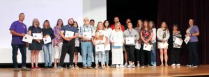 several adults pose on stage with certificates of achievement