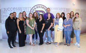 staff members pose in front of a school logo