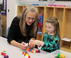 a woman sits at a table with a young student using building blocks