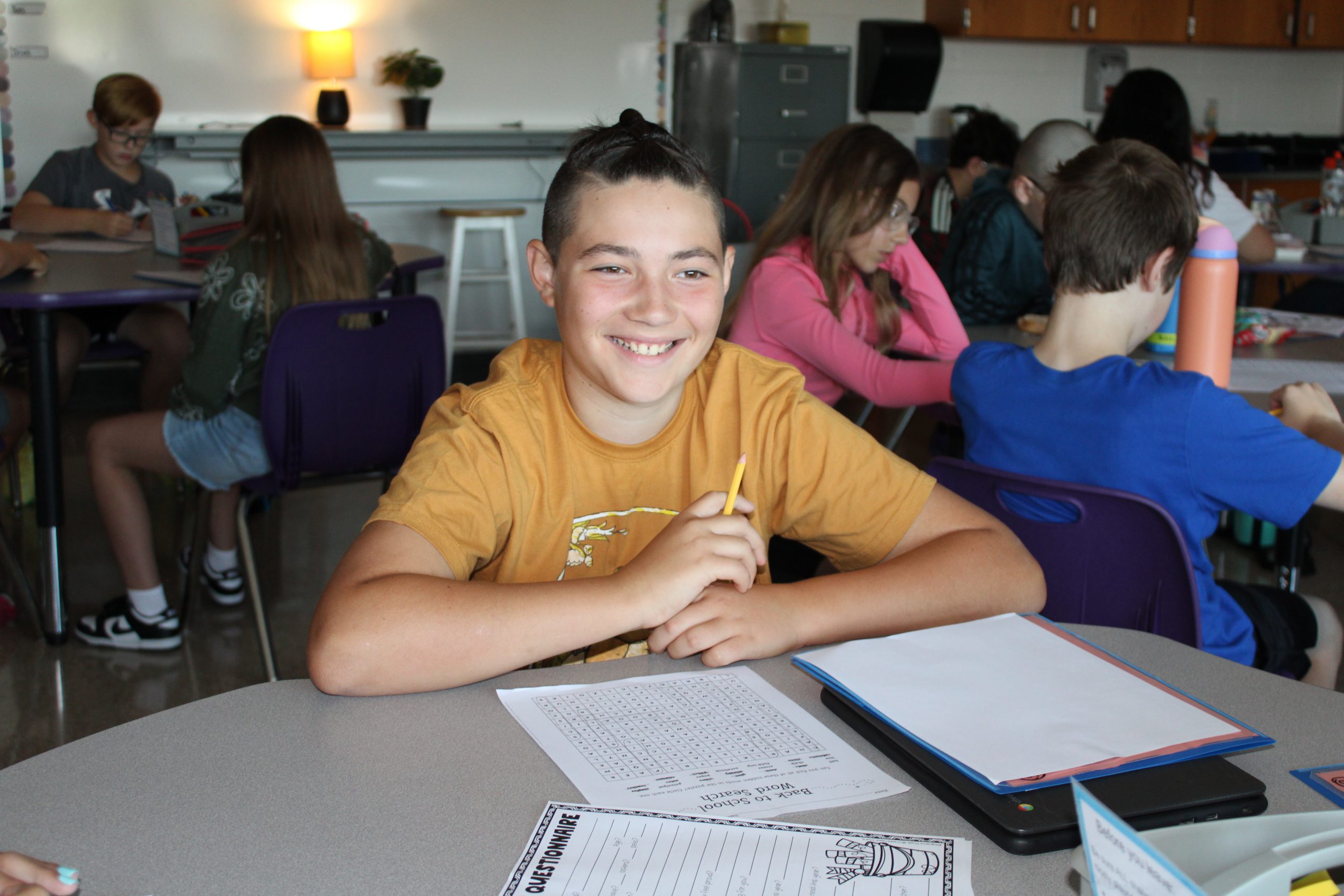 a young boy smiles while sitting at a desk and writing on paper