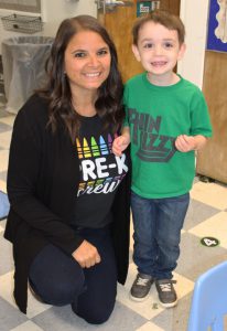 a teacher wearing black kneels down next to a student wearing a green t-shrt