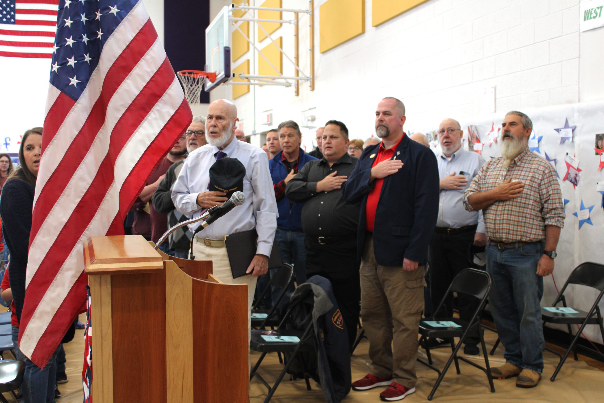 military veterans salute the flag at an assembly inside a gymnasium