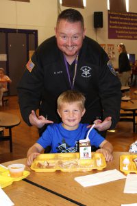 a man poses with a young boy in the cafeteria of a school