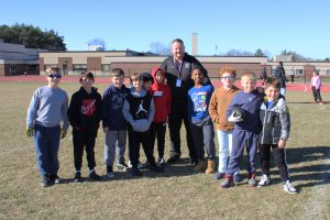 a man poses outside on a field with several elementary aged boys