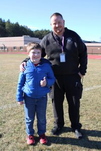 a man poses with a child outside on an athletic field