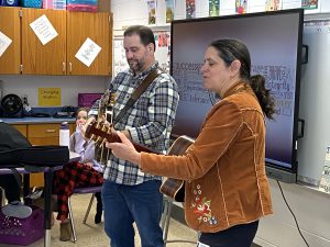 a man and a woman play guitar in a classroom